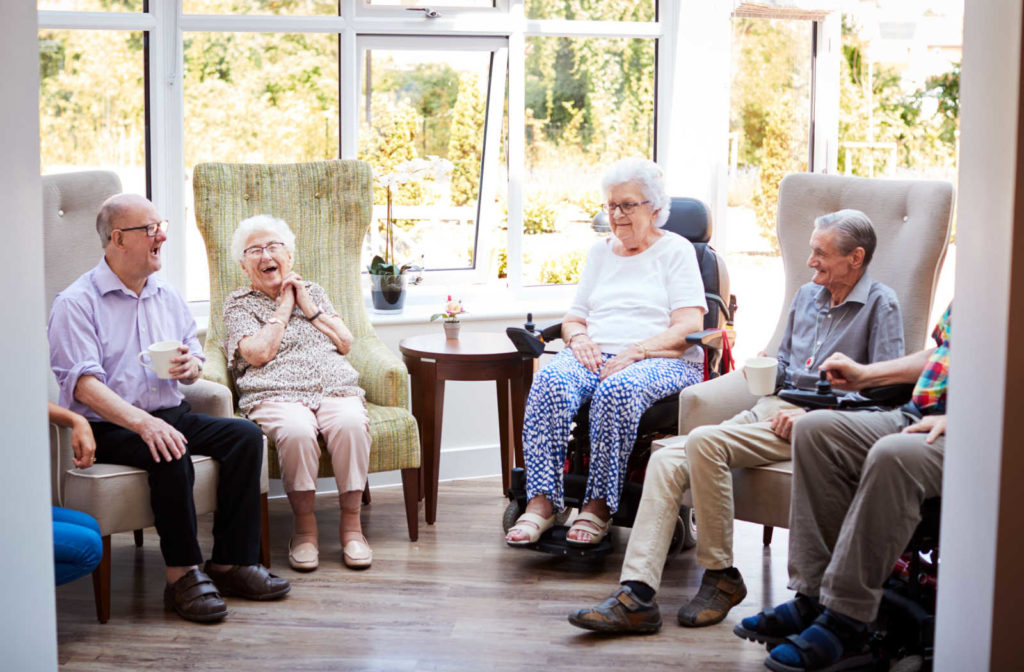 A group of seniors sitting talking to each other and having a cup of tea in a senior living community.