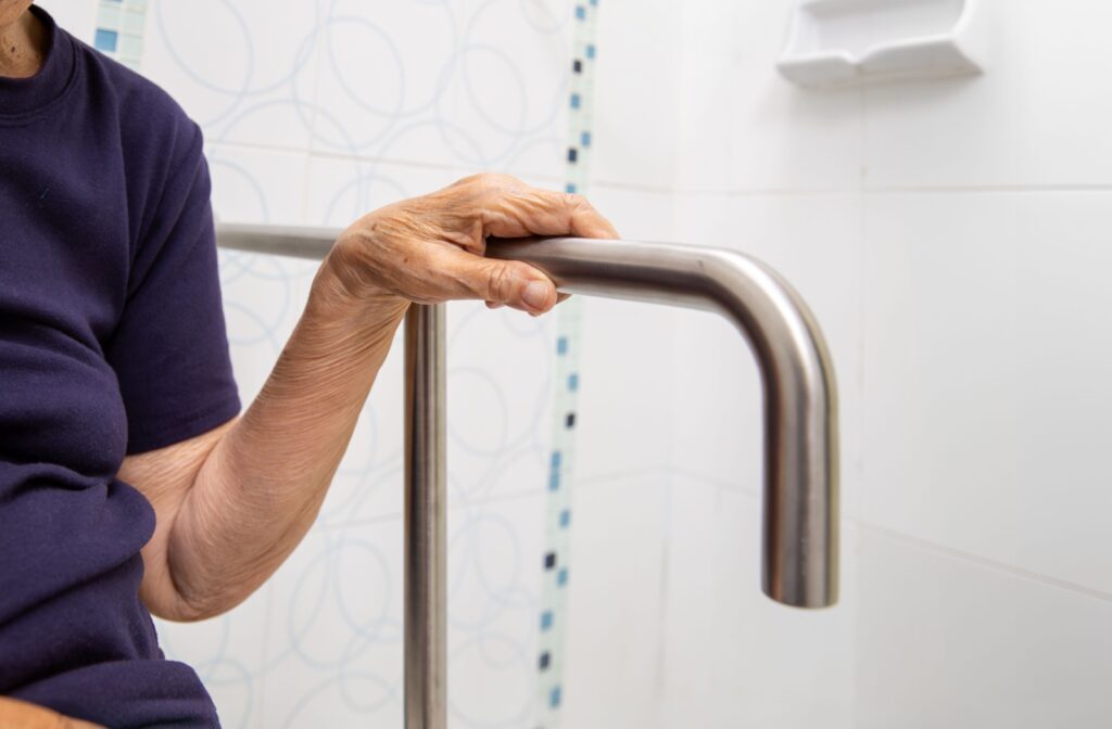 An older adult grips a sturdy handrail in a bathroom for support and stability.