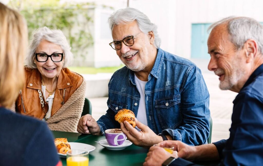 A group of seniors sit together at a table in their assisted living community for breakfast and coffee.