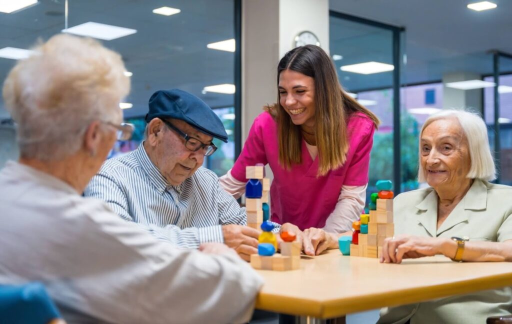 A nurse looks on as a group of older adults play a game in the shared space of their memory care community.
