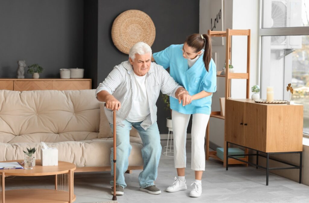 A friendly caregiver offers support to an older adult as they stand up with a cane.